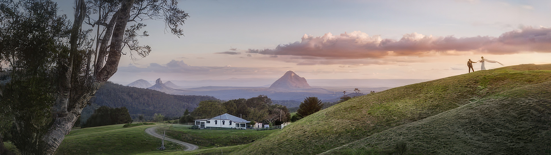A couple on the hilltop at On The View at sunset, with the Glasshouse Mountains beyond